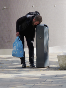 908303 Afbeelding van een jongeman die lege blikjes en flesjes zoekt in een afvalbak op het Jaarbeursplein te ...